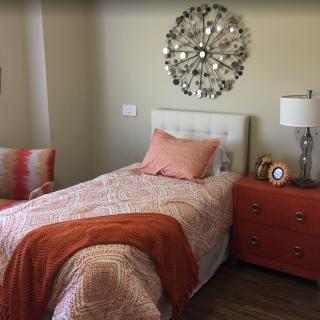 A cozy bedroom with a single bed, adorned with orange accents and stylish decor.