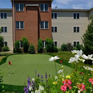A residential building with a landscaped area featuring a small golf putting green and colorful flowers.