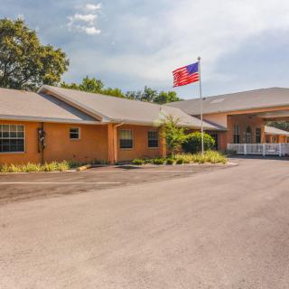 A single-story building with a flagpole in front, located next to a parking lot and surrounded by trees, under a partly cloudy sky.