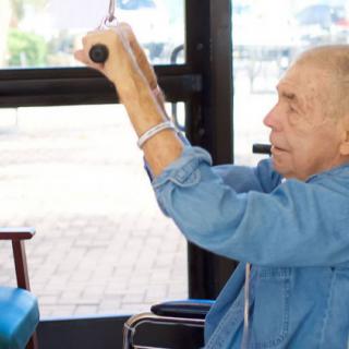 An elderly man in a wheelchair holds onto a handle inside a bus.