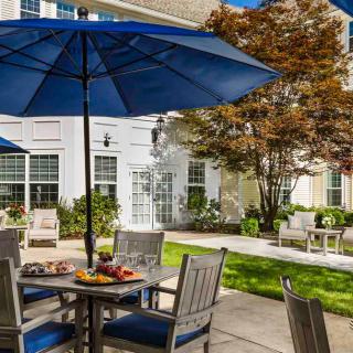 A sunny outdoor patio with blue umbrellas and garden furniture in a landscaped setting.
