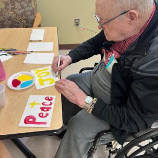 An elderly man enjoying a creative moment, painting colorful messages of peace at a table.
