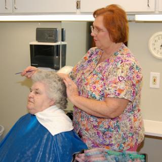 A hairdresser gives a haircut to a senior woman in a cozy salon setting.