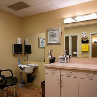 A makeup room with a large mirror, a chair, and a countertop featuring various items.