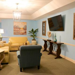 A cozy living room with blue walls, featuring a yellow sofa, blue armchair, flat-screen TV, and decorative elements including wall art and a potted plant.