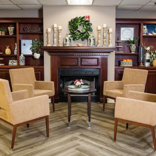 A cozy living room with four beige chairs arranged around a small table in front of a fireplace, adorned with decorative items and greenery.