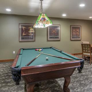 A cozy game room featuring a billiards table under stylish lighting fixtures, with framed artwork adorning the walls.