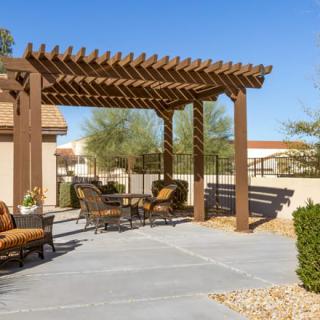 A sunny backyard featuring a wooden pergola with outdoor seating.
