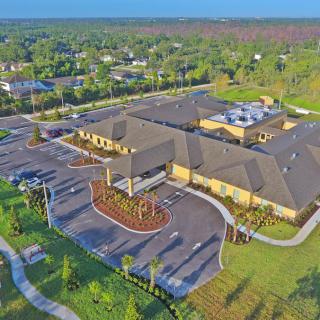 Aerial view of a large building complex surrounded by greenery and a parking lot.