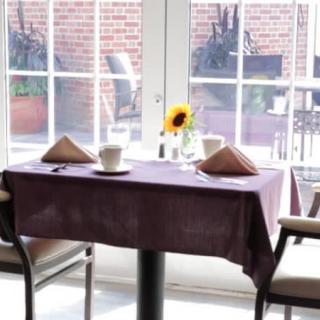 A neatly set dining table with a sunflower centerpiece by a large window.