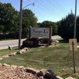 Welcome sign for a residential area along a road, surrounded by greenery.