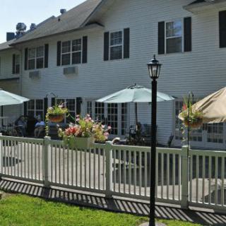 A view of a house with a patio area featuring umbrellas, outdoor seating, and a surrounding white fence.