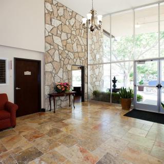 A spacious lobby with a stone wall, tiled flooring, and elegant furniture, leading to a glass entrance.
