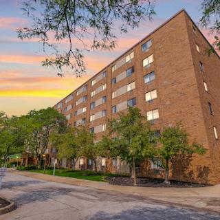 A modern brick apartment building illuminated by the warm glow of sunset, bordered by lush greenery.