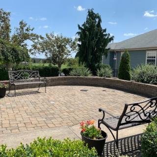 A serene outdoor patio area with benches and lush greenery under a clear blue sky.