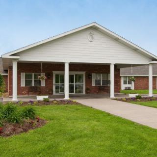 A single-story brick building with a well-maintained lawn and entrance supported by columns.