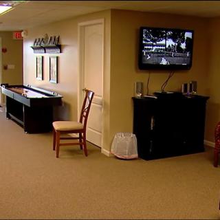 A cozy basement game room with a shuffleboard table and a mounted television.