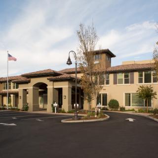 A modern building with a prominent entrance, surrounded by a parking lot and landscaped trees.