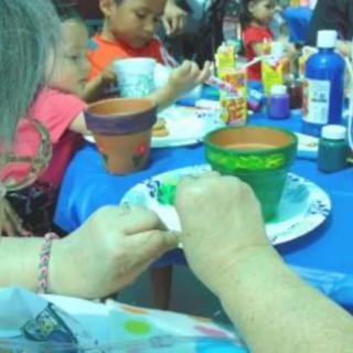 Children and adults gathered around a table engaged in a pottery painting session.