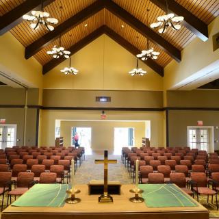 Interior view of a church with pews and an altar, featuring a prominent cross.