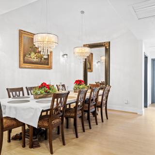 A spacious dining room featuring a long table with wooden chairs, illuminated by elegant chandeliers and adorned with decorative flowers.