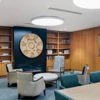 A modern office space with a seating area, bookshelves, and a large decorative clock on the wall.