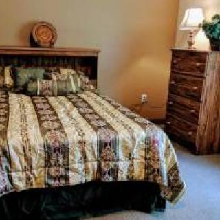 A cozy bedroom featuring a bed with a patterned comforter, a wooden dresser, and a lamp.