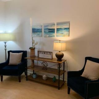 A cozy living room setup with two chairs, a small table adorned with lamps and decorations, and artwork on the wall.