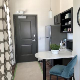 A modern kitchen area in an apartment featuring a refrigerator, bar stool, and decorative items.