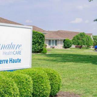 A healthcare facility sign with a building and greenery in the background.