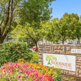 A beautifully landscaped entrance to the Woodside apartment complex, featuring colorful flowers and lush trees.