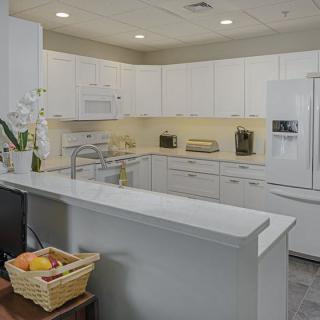 A modern kitchen with white cabinets and a clean countertop, featuring appliances and a fruit basket.