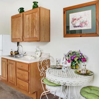 Cozy kitchen corner with wooden cabinets, a small sink, and a quaint dining area adorned with flowers and a decorative painting.
