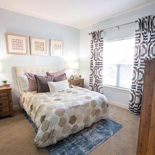 A cozy and well-decorated bedroom with a bed, wooden nightstands, patterned curtains, and framed artwork on the wall.