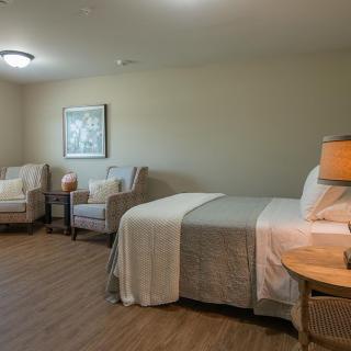 A cozy bedroom with a neatly made bed, two chairs, and warm lighting.