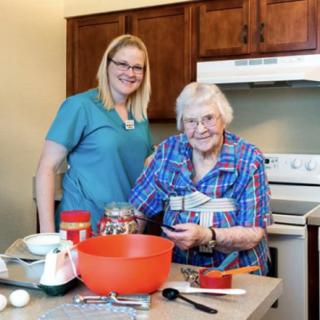 Two women smiling while preparing food in a kitchen.