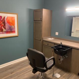 A modern salon room with a styling chair, sink, and wall artwork.