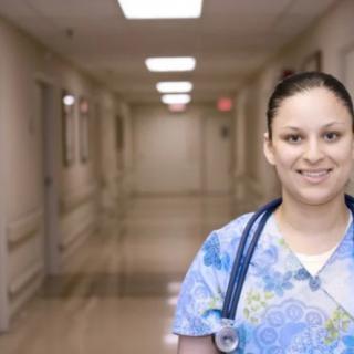 A nurse stands in a hospital hallway with a stethoscope around her neck.