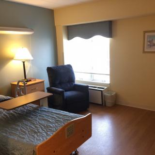 A simple hospital room with a bed, chair, and lamp near a window.