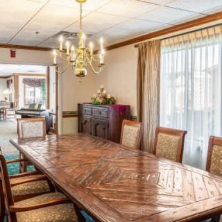 A well-lit dining room with a large wooden table, surrounded by chairs and a chandelier overhead.