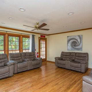 A cozy living room with comfortable sofas, hardwood flooring, a ceiling fan, and large windows.
