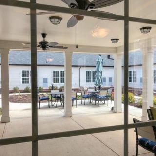 A cozy patio area with outdoor seating, ceiling fans, and protective columns under a covered roof.
