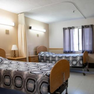 A shared hospital room with two beds, separated by a curtain and lit by natural light through a window.
