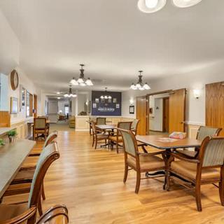 A spacious dining area with wooden floors and various tables and chairs arranged neatly under elegant lighting fixtures.