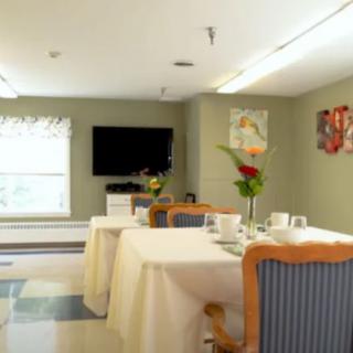 A dining room with neatly arranged tables and chairs, featuring a television and floral decorations.
