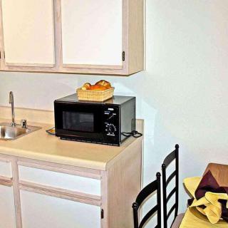 A small kitchen area featuring a microwave on the countertop, surrounded by cabinets and a dining table with chairs.