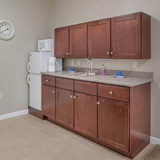 A small kitchenette with wooden cabinets, a refrigerator, microwave, and sink.
