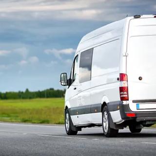 A white van driving on a rural road with a scenic background.