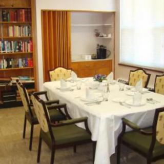 A dining room with a table set for a meal, surrounded by chairs and adjacent to a bookshelf.