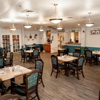 A spacious and elegantly decorated dining room with multiple tables and chairs, featuring soft lighting and wooden flooring.